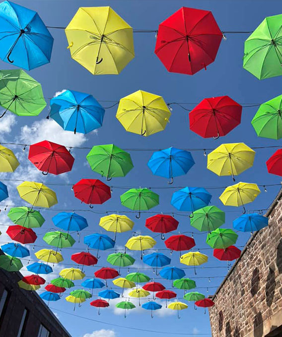 Photo of yellow, green, red, and blue umbrellas hanging in the sky between buildings