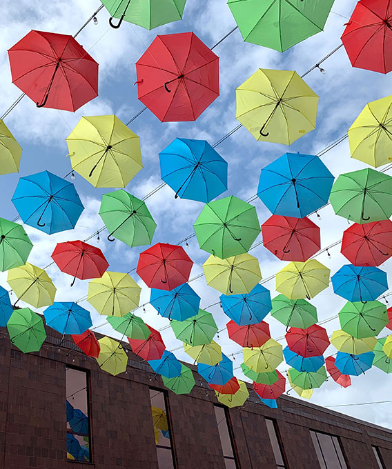 Photo of yellow, green, red, and blue umbrellas hanging in the sky between buildings