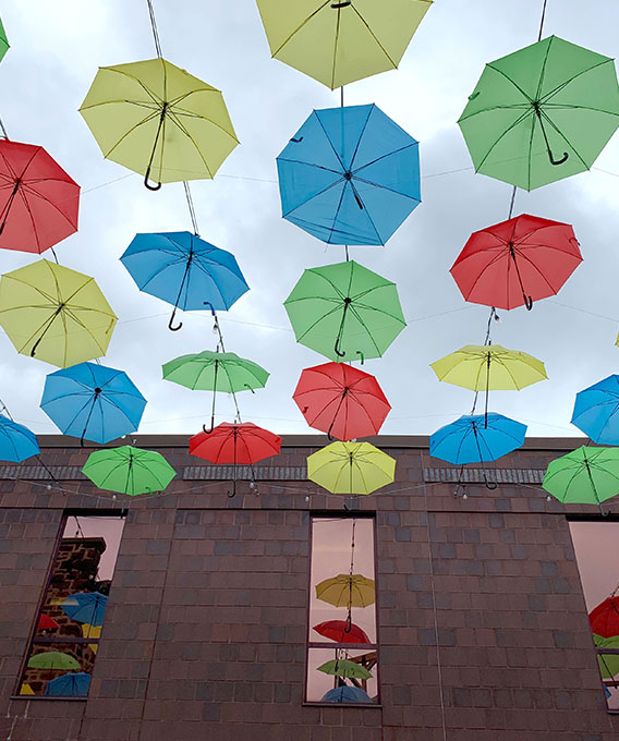 Photo of yellow, green, red, and blue umbrellas hanging in the sky between buildings