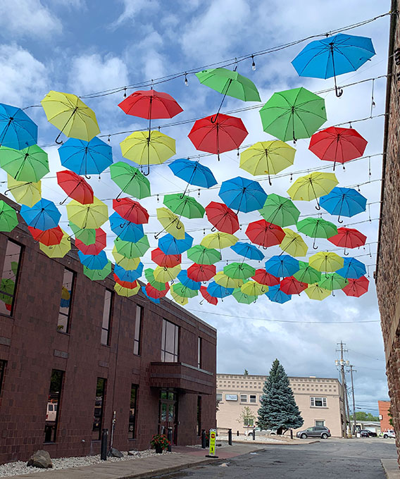 Photo of yellow, green, red, and blue umbrellas hanging in the sky between buildings