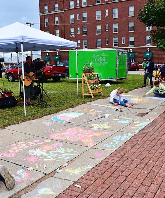 People drawing with sidewalk chalk in front of a man playing guitar