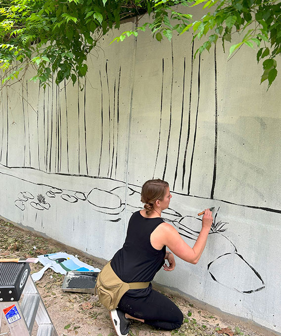 Woman painting a mural of rocks and trees