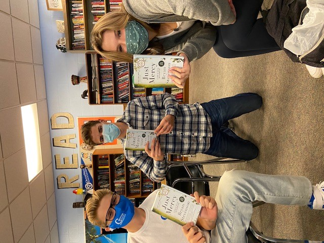 Three masked young people holding copies of a book