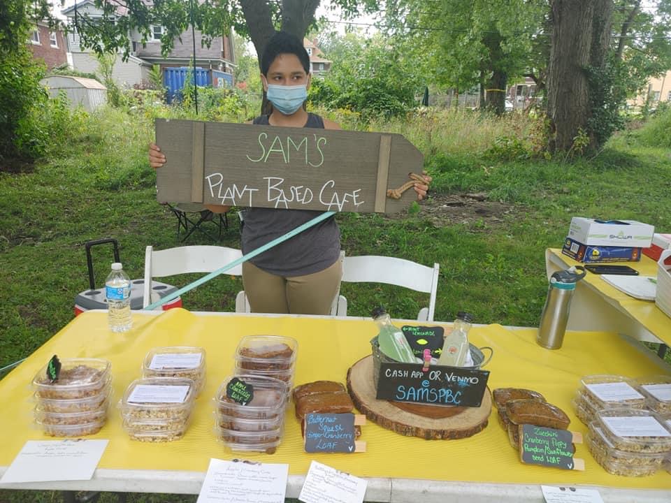 Photo of a man holding a sign for Sam's Plant Based Cafe