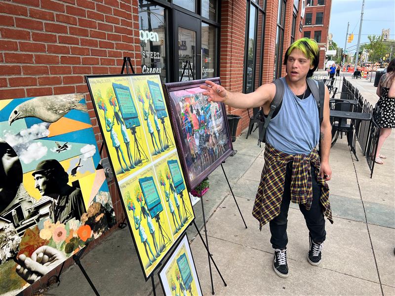 Person pointing at art work on easles along a sidewalk