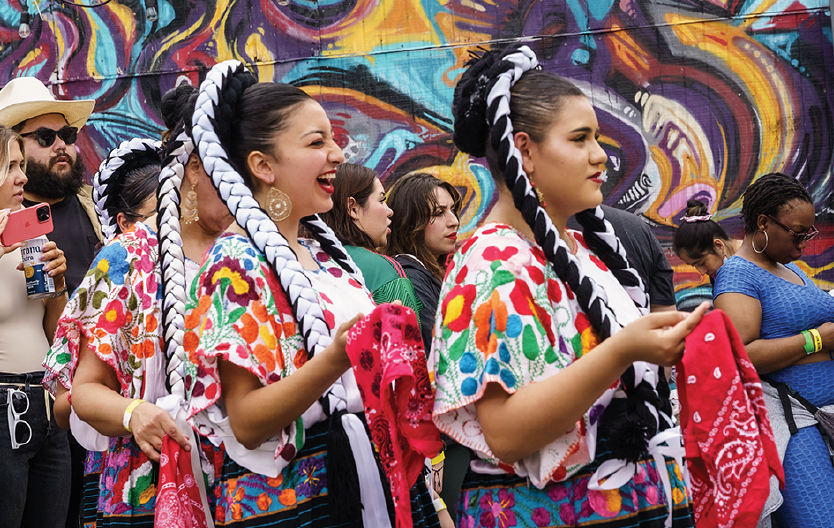 Women smiling in colorful costumes in front of a mural